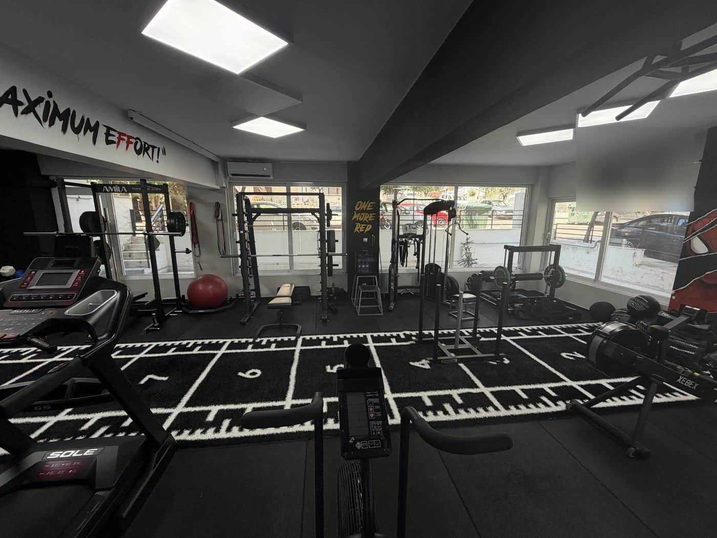 Ο χώρος με φυσικό φως — smith machine, racks και ο τοίχος «One More Rep»
